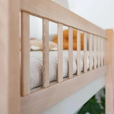 Zbliżenie na drewnianą barierkę górnego poziomu łóżka piętrowego